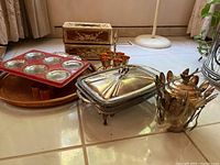 Photo of silver plated covered dish, stainless steel coasters, plastic tissue box holders, metal muffin tin, vintage jewelry box, copper napkin rings