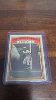 Photo of a 1972 Topps Roberto Clemente baseball card in a plastic protective sleeve, showing the front of the card with Clemente in a batting pose and '1971 World Series Game No.4' text.