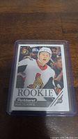 Photo of Brady Tkachuk rookie card in a protective plastic sleeve on wooden surface.