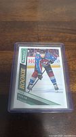Front view of Cale Makar rookie hockey card in protective plastic case on wooden surface.