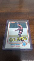 Photo showing the Jari Kurri rookie card in a protective sleeve on a wooden surface, capturing the front design and details.
