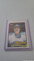 Close-up photo of Randy Johnson rookie baseball card in protective plastic sleeve showing front side with player portrait and Mariners team logo.