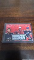 Photo of a Wayne Gretzky collectible card with 'MAN-MYTH-LEGEND' title, three images of Gretzky, and facsimile autograph, encased in clear protective plastic on a wooden surface.