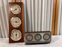 Pair photo showing tall Sunbeam wooden weather station alongside smaller Springfield rectangular weather station