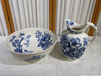 Both basin and pitcher shown together on a table with white cloth background, highlighting blue and white floral ceramic design.
