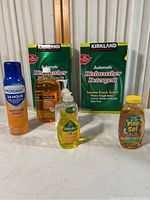 Full view of all cleaning products including Kirkland dishwasher detergents, Pine-Sol cleaner, Palmolive dish soap, Spa Soap hand soap, and Microban sanitizing spray on table.