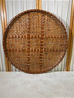 Full view of the large, flat, round wicker basket showing woven lattice pattern and rim.