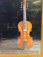 Full view of the framed poster showing the decorated violin and background text.