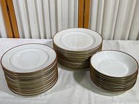 Photo showing 3 stacks of dinnerware: 10 dinner plates, 11 salad plates, and 10 bowls all with gold rims.