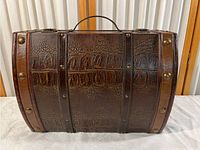 Front view of brown embossed leather carrying case with brass rivets and decorative wooden rim accents.