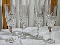 Four clear crystal champagne flutes standing upright on a white cloth background, showing etched diamond and starburst patterns on each glass.