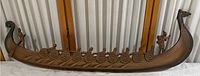 Full view of the wooden Viking longship with shields and rowers from a slightly angled perspective. Mounted on a vertical slatted white background.