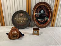 Lot setup showing both beer signs, pirate head wall ornament, and small framed item on white cloth.