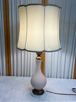 Side view showing entire lamp with scalloped white fabric shade illuminated.