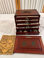 Mahjong tile rack with drawers, wooden cover panel, and instruction booklet displayed on table.