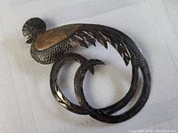 Front view of the silver peacock brooch showing detailed feather engraving and gold-tone accent on wing.