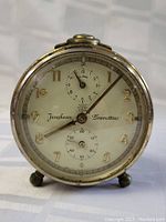 Front view of the Junghans Bravettino clock showing the dial with gold-tone Arabic numerals, two subdials, and visible metal casing with feet.