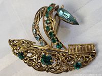 Close-up side-angle photo of brooch showing green stones and filigree details