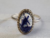 Close-up front view of early sterling silver ring with oval Delft blue porcelain center showing a windmill, set in textured silver bezel.