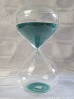 Full view of a clear glass hourglass filled with green sand, showing sand gathered in the top portion, ready to flow down.