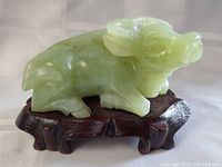 Side view of light green jade water buffalo carving on dark wooden stand