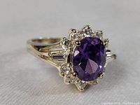 Close-up of sterling silver ring showing oval amethyst center and clear stones halo with baguette accents.