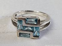 Front view of sterling silver ring featuring five aqua marine stones in a geometric formation on a split band. Ring surface and stones in good condition.