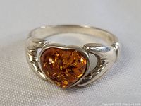 Close up of the sterling silver Claddagh ring showing the heart-shaped amber stone centered between two hands and topped by a crown.