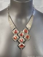 Front view of hammered sterling silver necklace with a cluster of seven red cabochon stones arranged in geometric settings suspended by chain links.