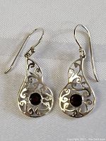 Front view of matching pair of sterling silver earrings featuring open filigree design and deep red garnet stones set in center.