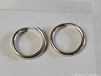Pair of sterling silver hoop earrings laid on a white textured fabric showing full round hoops with hinged closure.