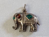 Front view of the sterling silver elephant pendant charm showing amber and green jeweled stones