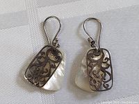 Pair of sterling silver drop earrings with mother of pearl and an intricate filigree overlay shown side by side on a white fabric background.