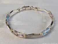 The sterling silver bracelet displayed flat, showcasing pink and blue stones alternating in a geometric setting, on a white fabric background.