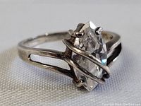 Close-up front angled view of sterling silver ring with marquise-cut diamond showing prongs and swirl design on band.