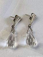 Pair of sterling silver drop earrings with faceted clear Swarovski crystal drops on white fabric background.