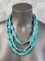 Front view of the three-strand turquoise necklace displayed on a mannequin bust, showing the polished oval turquoise beads with white veining and small white round beads between them.