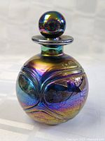 Front view showing round bottle with swirling raised glass pattern and multi-color iridescent finish.