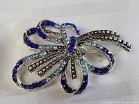 Brooch pin laying flat on a white textured surface displaying front view with clear details of blue rhinestones and silver-tone beads.
