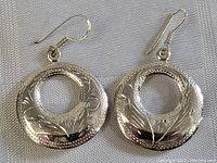 Pair of vintage sterling silver earrings with carved floral donut design and hooks on a white fabric background