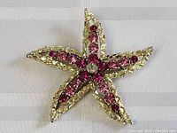 Starfish-shaped brooch viewed from a top angle showing five arms with pink and purple rhinestones and a clear central rhinestone on a textured gold-tone metal base.