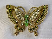 Photo showing close-up front view of the butterfly pin highlighting green and clear rhinestones on gold-tone filigree wings.