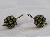 Front view of both earrings showing circular arrangement of green stones around square center stone and silver hooks.