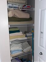 Photo of shelves showing folded wool blankets in beige, olive green, and cream tones along with stacks of bath towels, hand towels, face cloths, sheets, and pillow cases in white, cream, and light blue.