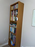 Front view showing the full height and shelving filled with books. The bookcase stands against a beige wall.