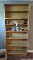 Front view of tall wooden bookcase with six shelves, showing some decorative items on shelves.