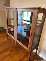 Front view showing two glass doors, wooden frame, and tapered legs
