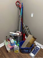 Wide view of cleaning equipment including mops, brushes, bucket, rugs, and cleaning supplies container.