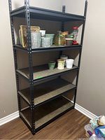 Full view of black metal frame storage shelf with flower pots and hummingbird feeder on shelves.