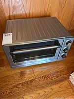 Stainless steel rectangular toaster oven with black handle on glass door and three control knobs on the right side.